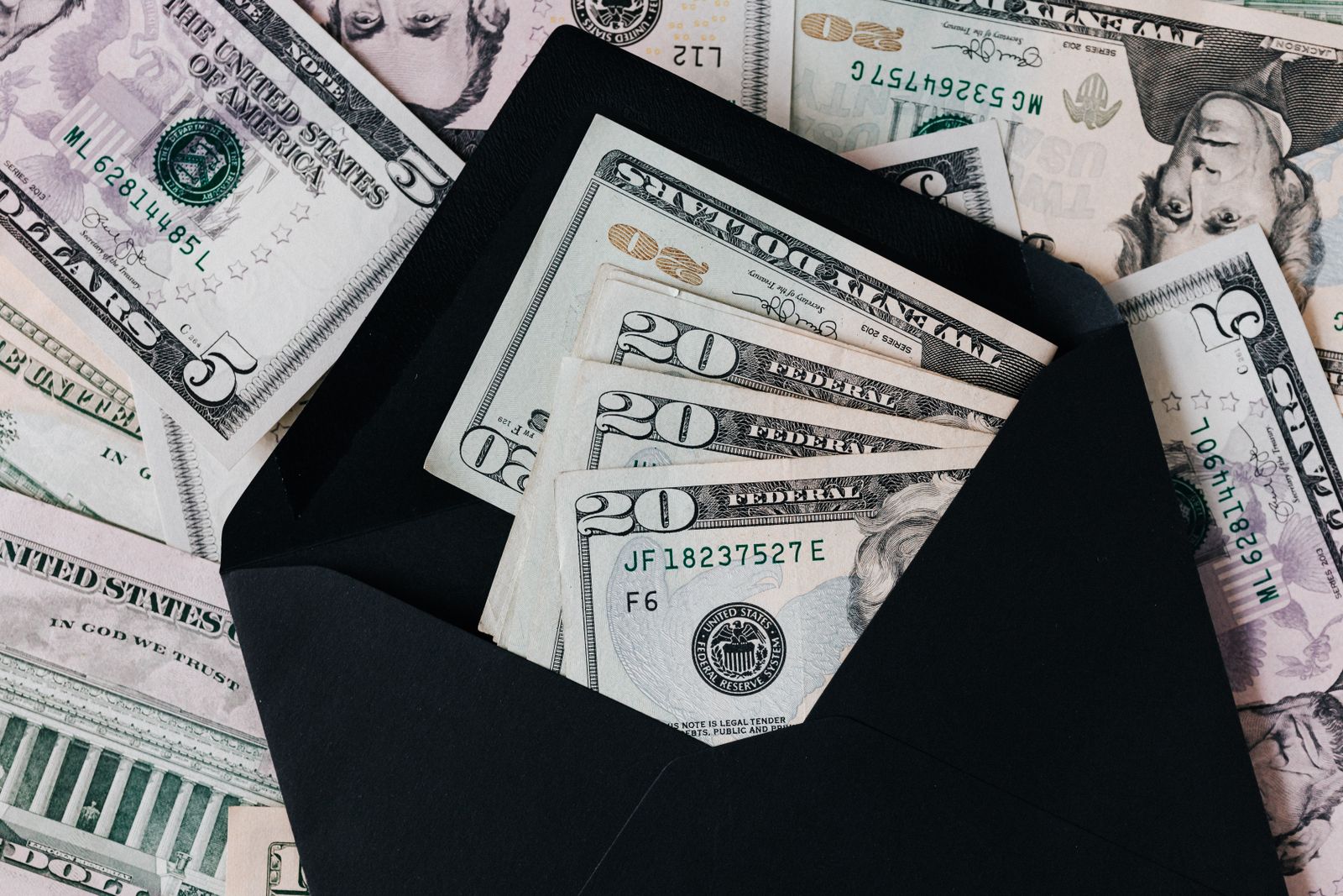 US dollar bills fanned out from a black envelope